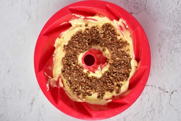 Bundt pan with cake batter, using the classic Sock it to us cake recipe with cake mix, topped with a crumble layer and placed on a textured light surface.