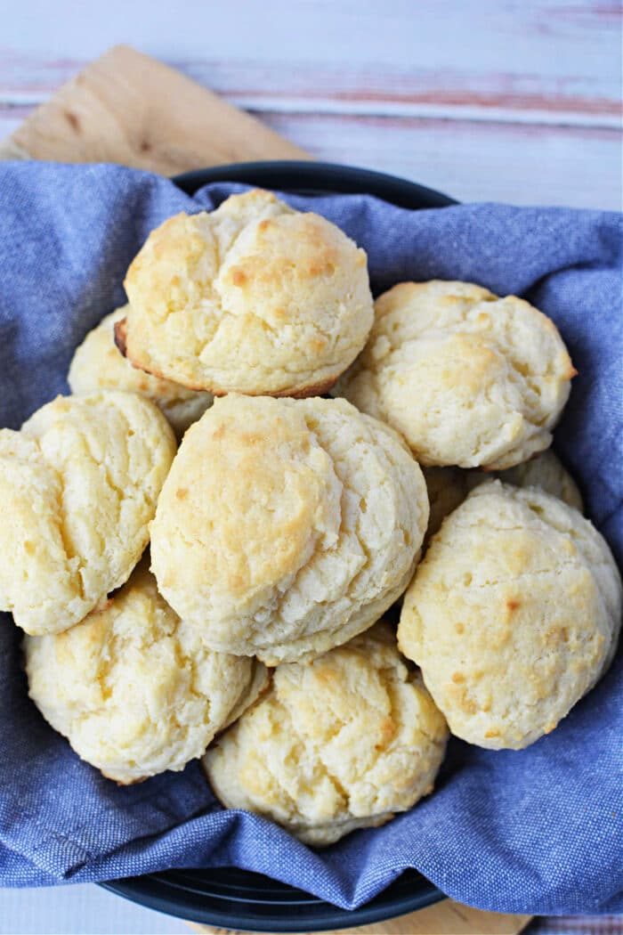A basket lined with blue cloth holds several golden, fluffy sour cream biscuits—a solid treat for anyone searching for the ultimate biscuits recipe.