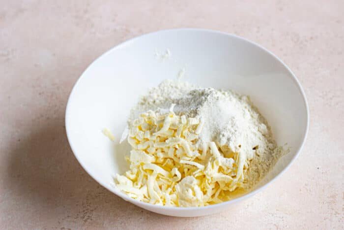 A white bowl brimming with shredded butter and flour rests on a light countertop, ready to craft the solid sourdough pie crust.