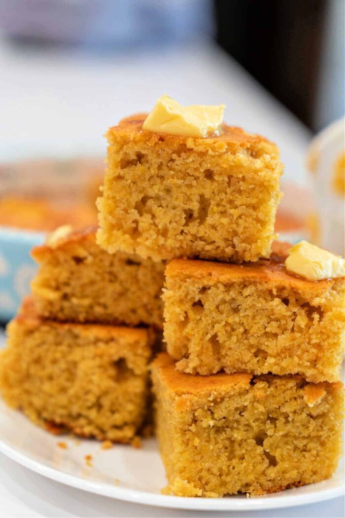 A stack of cornbread squares, a classic Southern dish often made with buttermilk and cornmeal, topped with melting butter on a white plate.