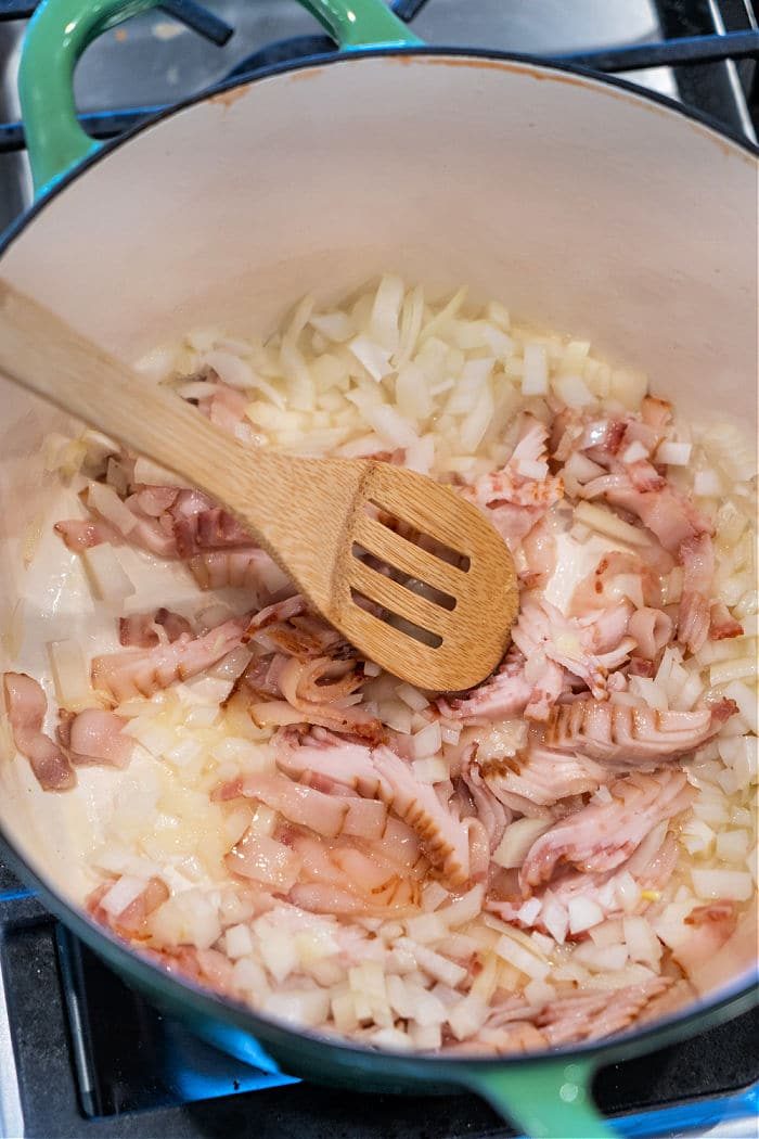 Chopped onions and bacon cooking in a pot with a wooden spoon on a stove—solid beginnings for classic Southern Fried Cabbage.