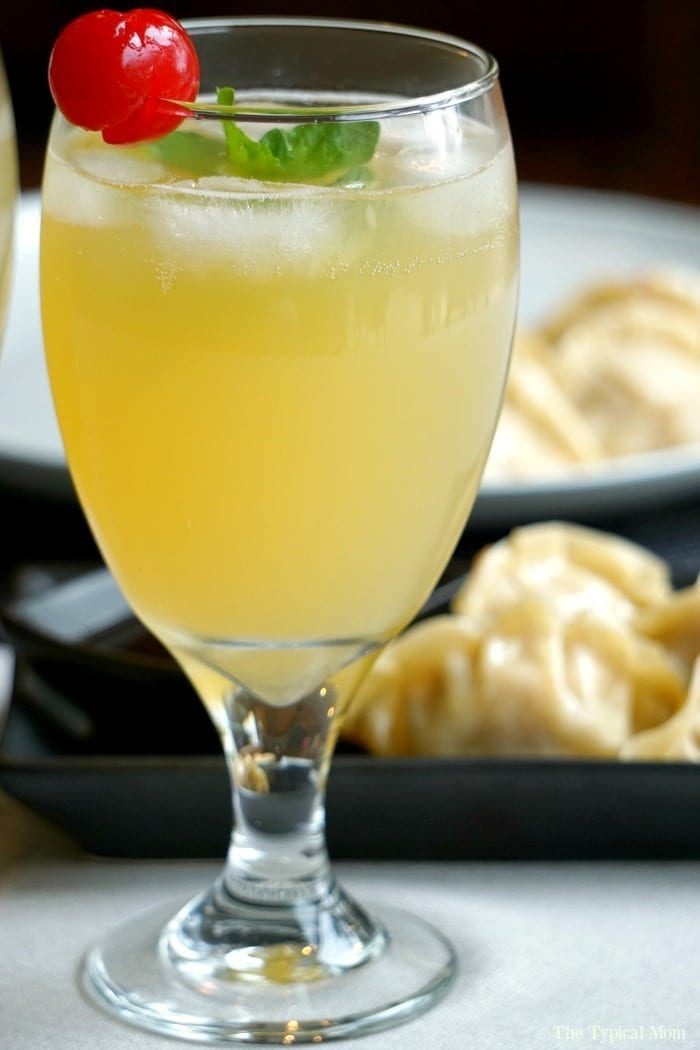 A glass of sparkling malibu by breeze, elegantly garnished with a cherry and mint, sits enticingly in the foreground, while savory dumplings temptingly linger in the background.