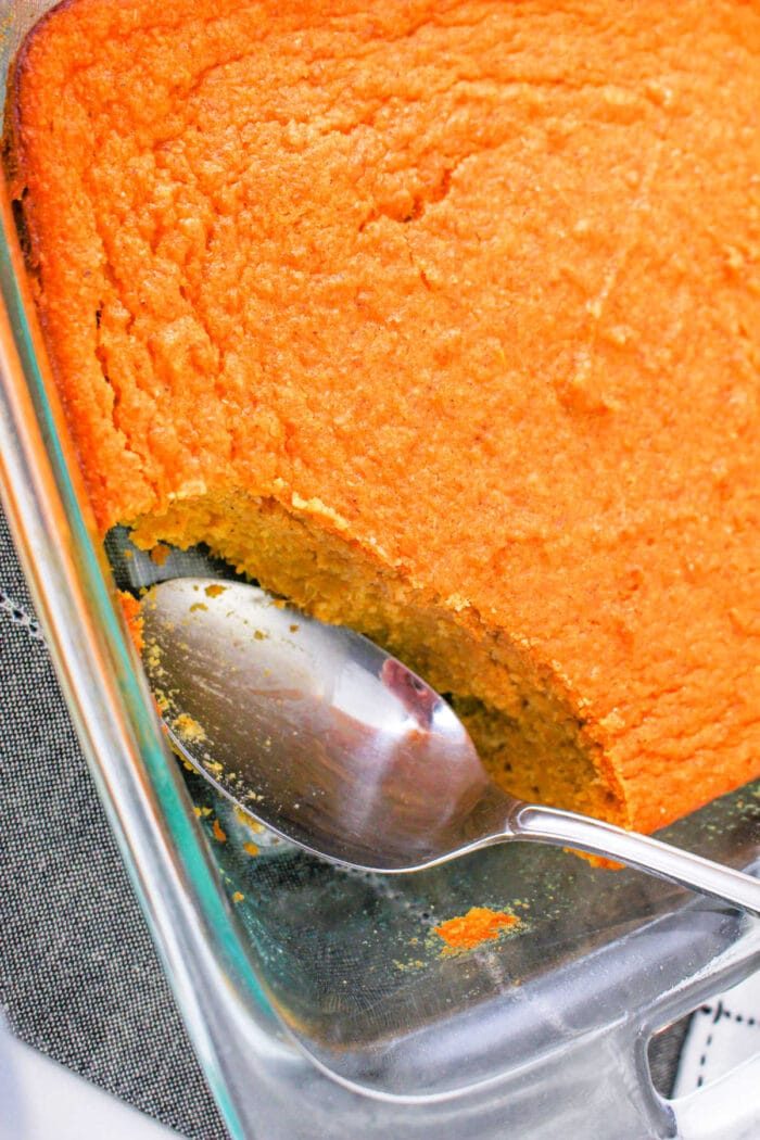 A glass dish showcases a baked spoonbread, partially scooped with a spoon—a delightful sweet potato spoonbread recipe waiting to be shared.