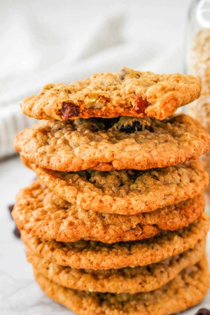A stack of steel cut oatmeal raisin cookies proudly sits on a white surface, with a jar of steel cut oats in the background.