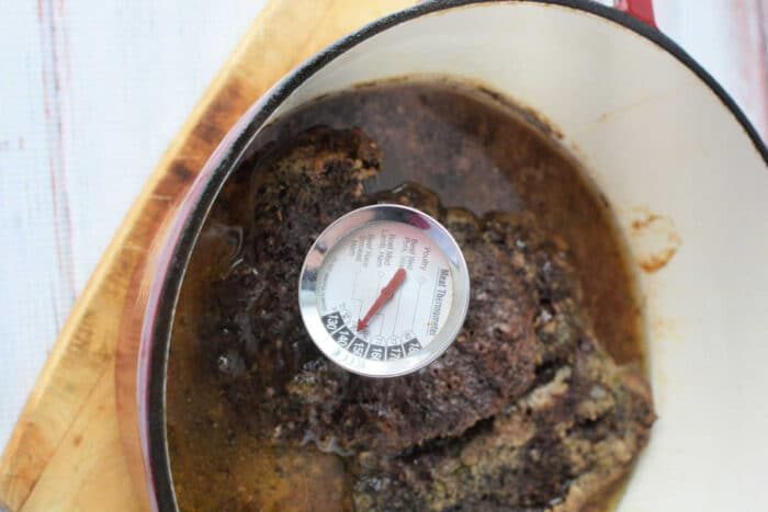 A succulent Stove Top Pot Roast sits in a pot on a wooden surface, with a thermometer revealing its solid temperature of 150 degrees Fahrenheit.