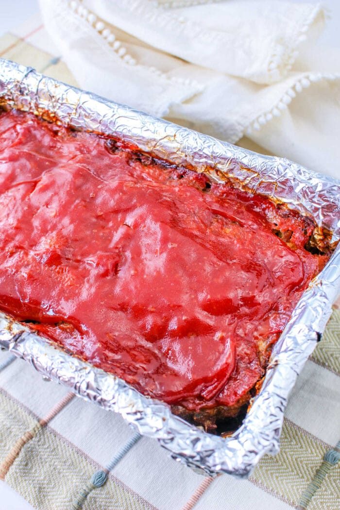 Stove Top Stuffing Meatloaf covered in glaze rests in a foil-lined pan on a plaid cloth.