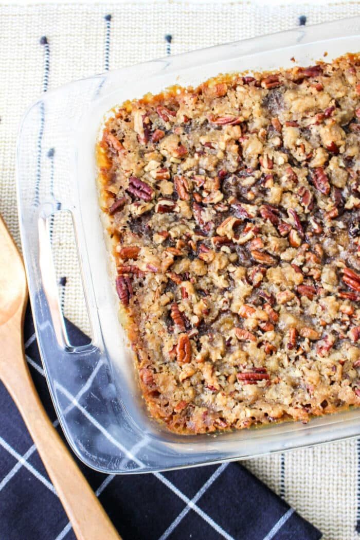 A glass baking dish with a freshly baked sweet potato casserole with canned yams, accompanied by rustic wooden cooking utensils.