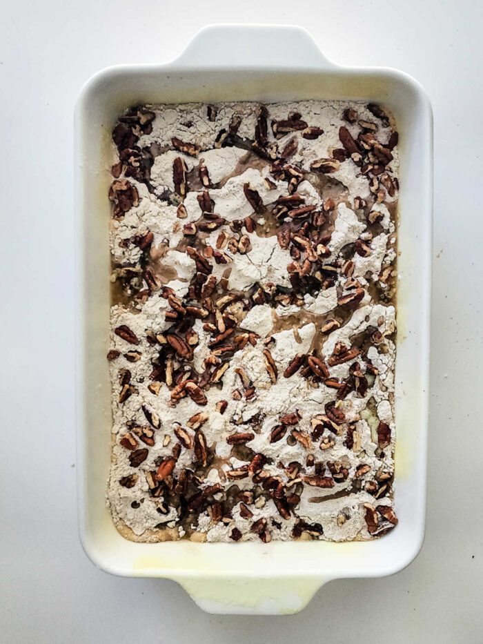 Rectangular baking dish with flour mixture and chopped pecans on top, ready to be baked into a good Sweet Potato Dump Cake.