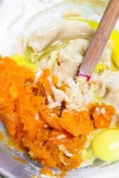 Mixing bowl containing raw ingredients: mashed orange sweet potato, an egg, and dough being combined with a wooden spoon for a delightful sweet potato muffin recipe.