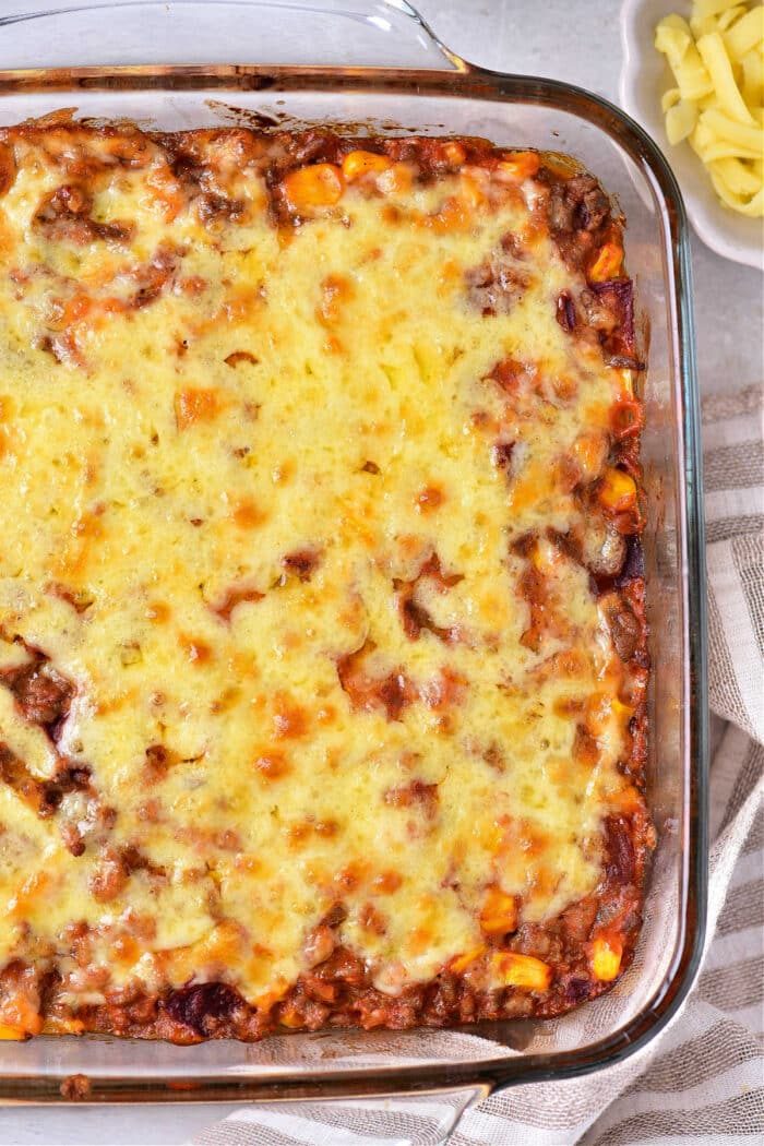 A Jiffy taco cornbread casserole topped with melted cheese in a glass dish, accompanied by sliced cheese on the side.