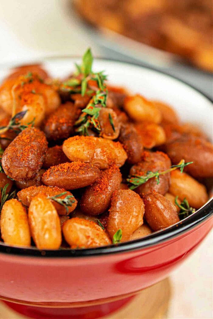 Close-up of seasoned baked tepary beans in a red bowl, garnished with sprigs of thyme.