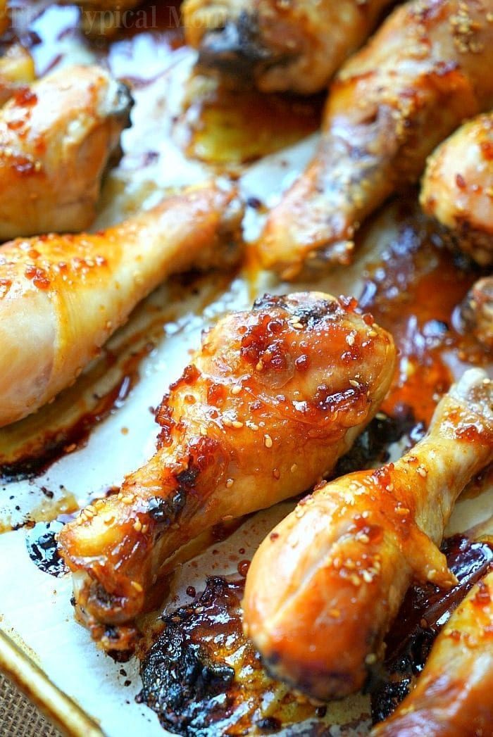 Close-up of teriyaki chicken drumsticks glazed with a sticky sauce, arranged on a baking tray. The drumsticks boast a golden-brown, crispy exterior with visible sesame seeds and caramelized edges.