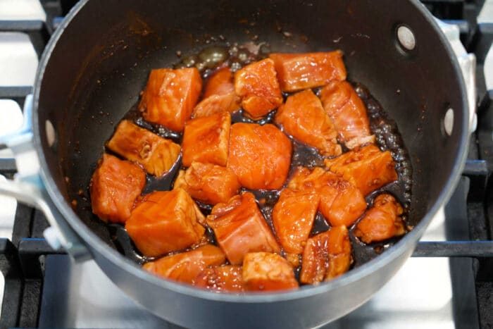 Chunks of salmon cooking in a dark teriyaki sauce in a saucepan on a stovetop—solid for a quick Teriyaki Salmon recipe or flavorful Salmon Bites.