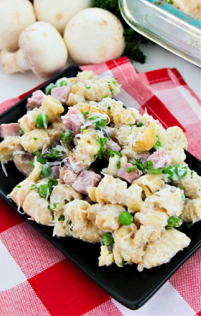 A delightful creamy pasta salad with leftover turkey, peas, and cheese sits on a checkered tablecloth, reminiscent of a classic tetrazzini recipe. Mushrooms add a touch of earthy elegance in the background.