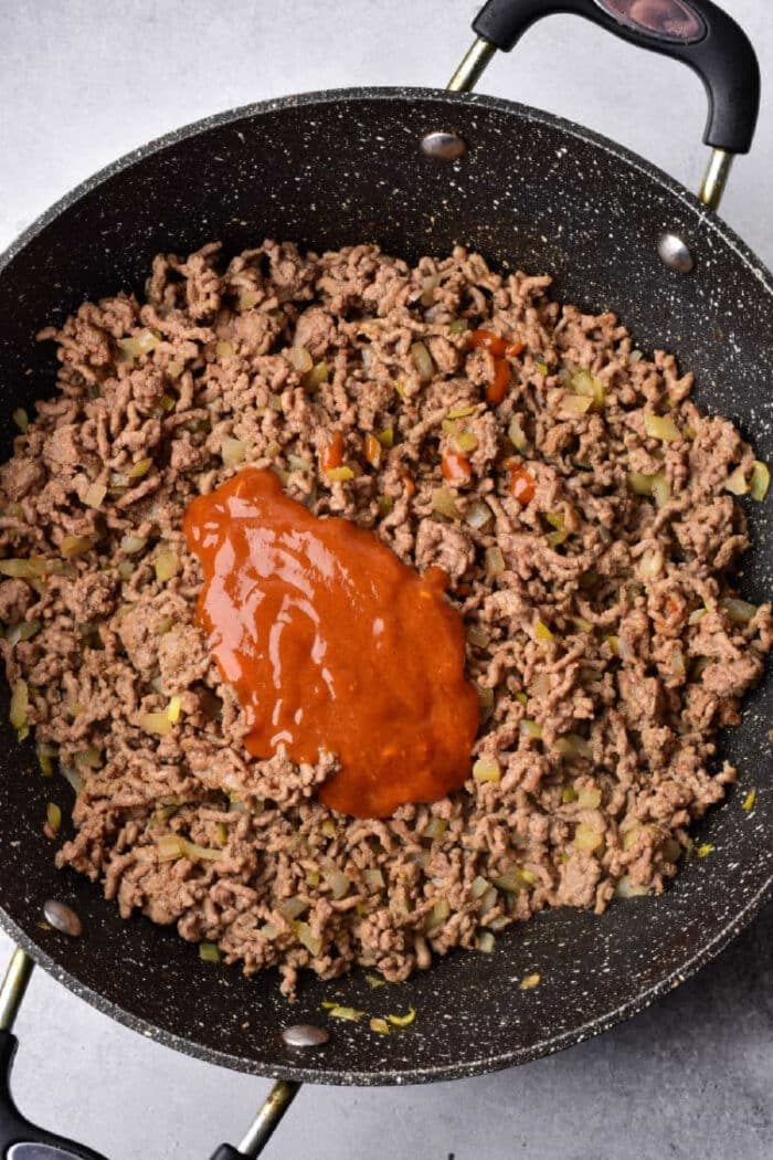 Ground beef and chopped onions sizzle in a skillet with rich red sauce on top—solid for piling onto Texas toast sloppy joes.