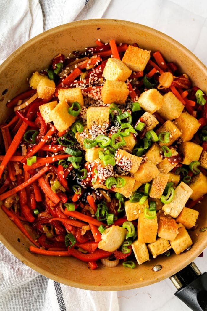 A skillet with tofu cubes, green onions, sesame seeds, mixed vegetables, and a touch of tofu for that lettuce wrap vibe.