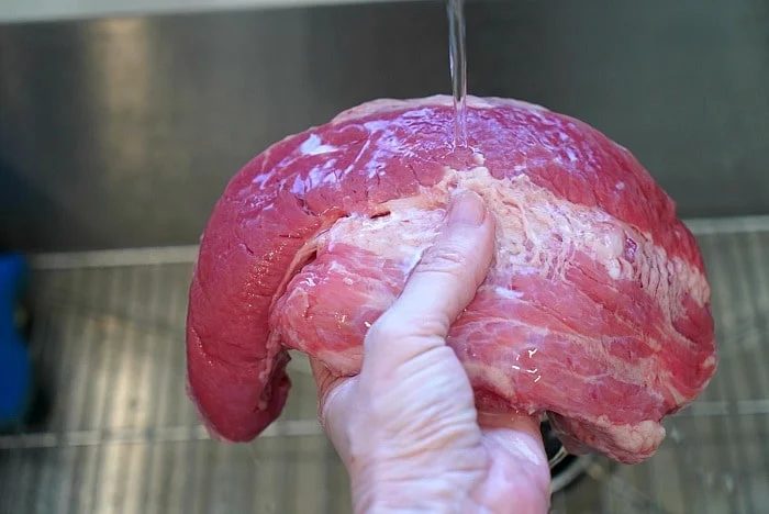 Carefully rinsing a large slab of point cut corned beef under running water in the kitchen sink, prepping it for a good meal.