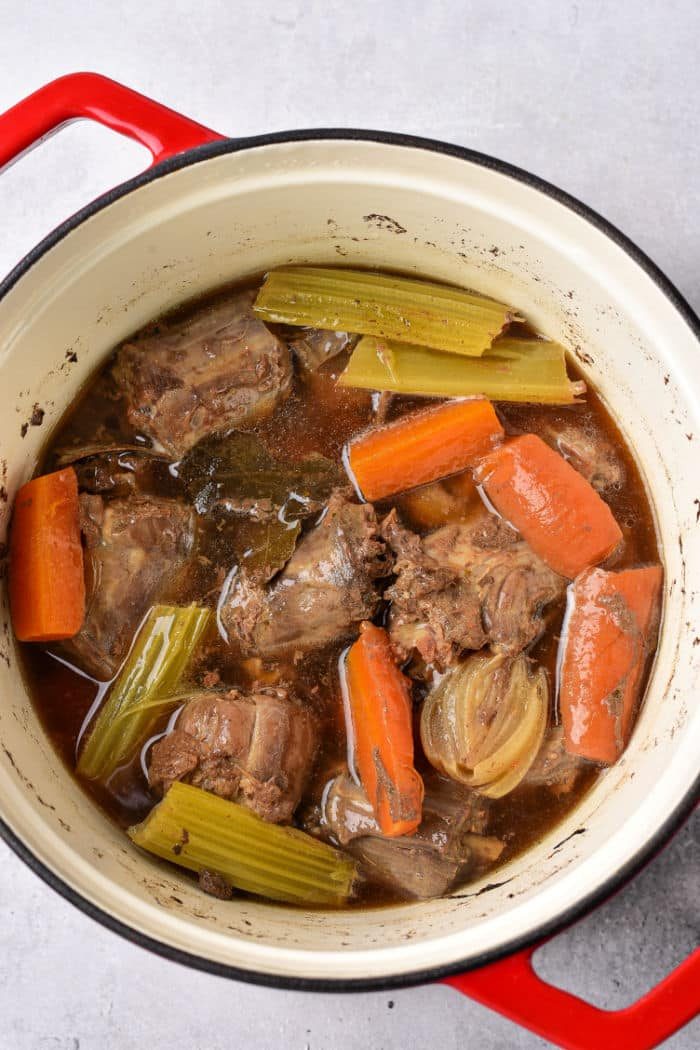 A pot of braised turkey necks, carrots, celery, onion, and broth simmering gently with a hint of turkey neck gravy for added richness.