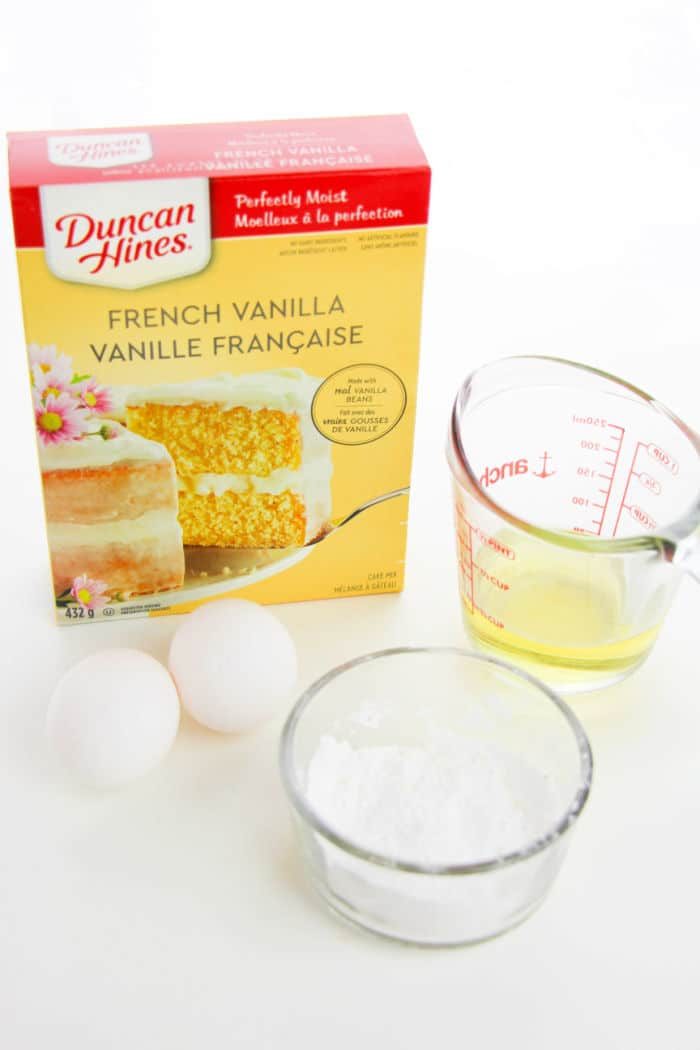 Box of French vanilla cake mix, two eggs, a measuring cup with egg whites, and a bowl of powdered sugar—everything you need for quick and good 3 Ingredient Cake Mix Cookies.