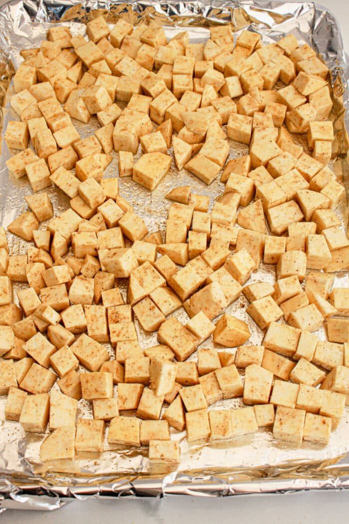 Cubed sweet potato seasoned and spread on a foil-lined baking sheet, ready to be baked—solid as a protein-packed addition to any White Sweet Potato Recipe.
