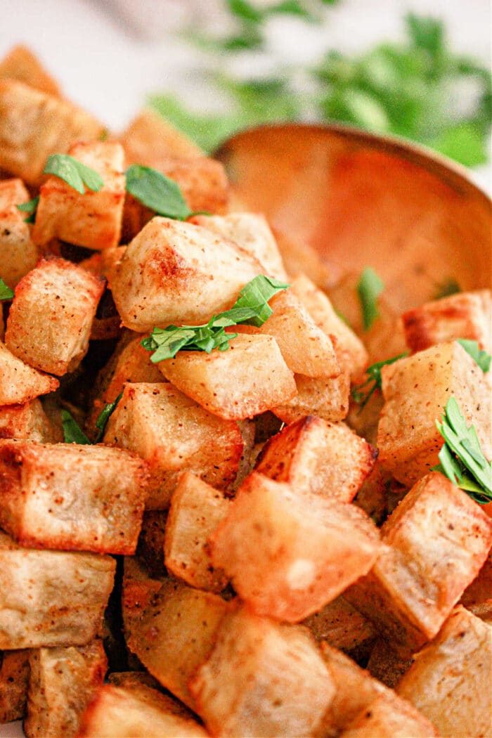 Crispy roasted white sweet potato cubes garnished with fresh parsley, with a wooden spoon in the background—a good white sweet potato recipe.