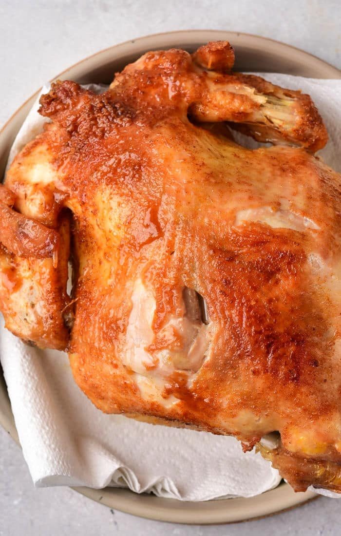 A roasted whole chicken with crispy, golden-brown skin rests on a paper towel-lined plate, echoing the mouthwatering allure of a whole fried chicken.
