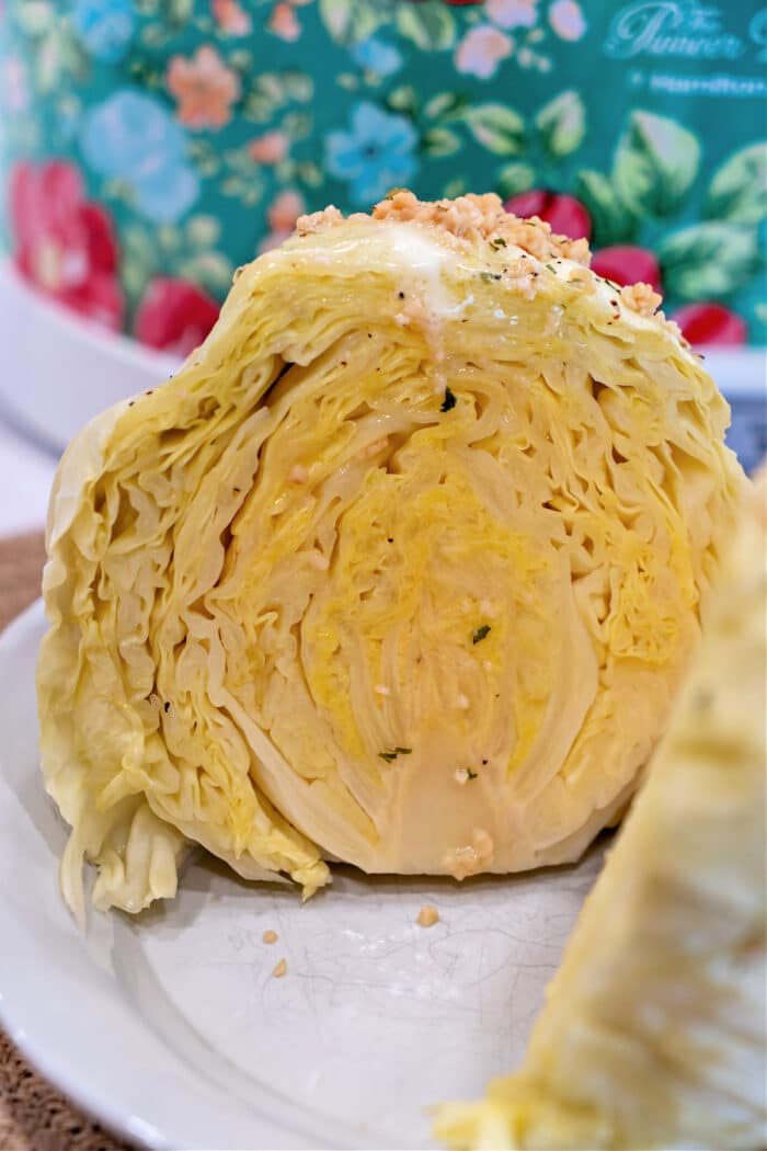 Close-up of a sliced cabbage on a plate, its layered texture and light yellow color beautifully contrasted against a colorful floral background, reminiscent of the tenderness achieved from cooking a whole head of cabbage in a slow cooker.
