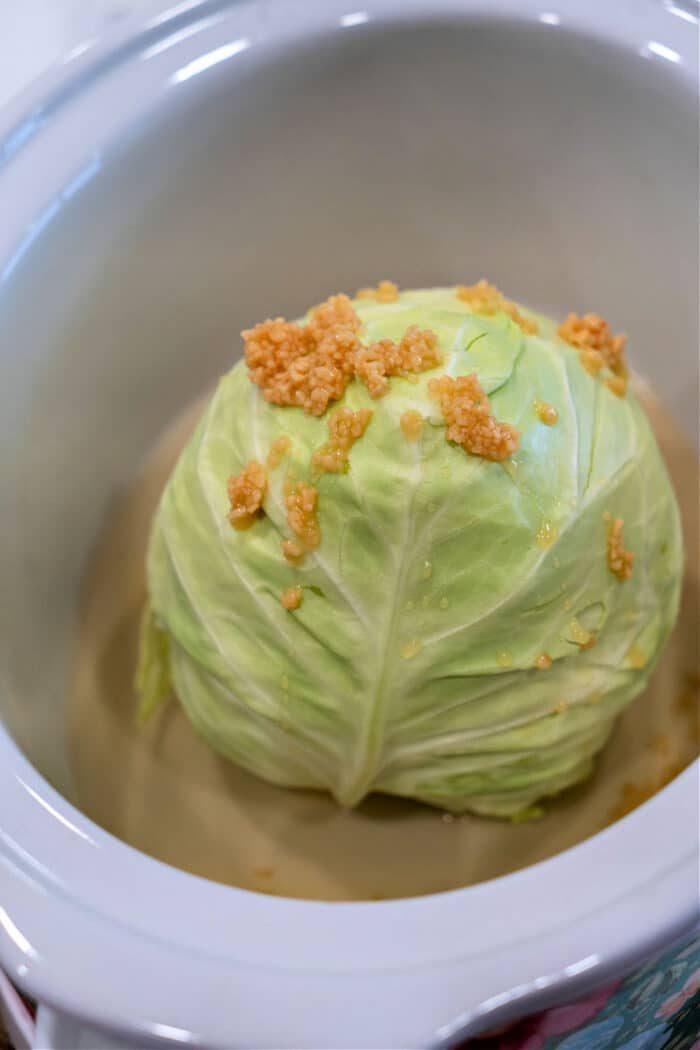 A whole head of cabbage in a slow cooker, delightfully topped with fragrant minced garlic.
