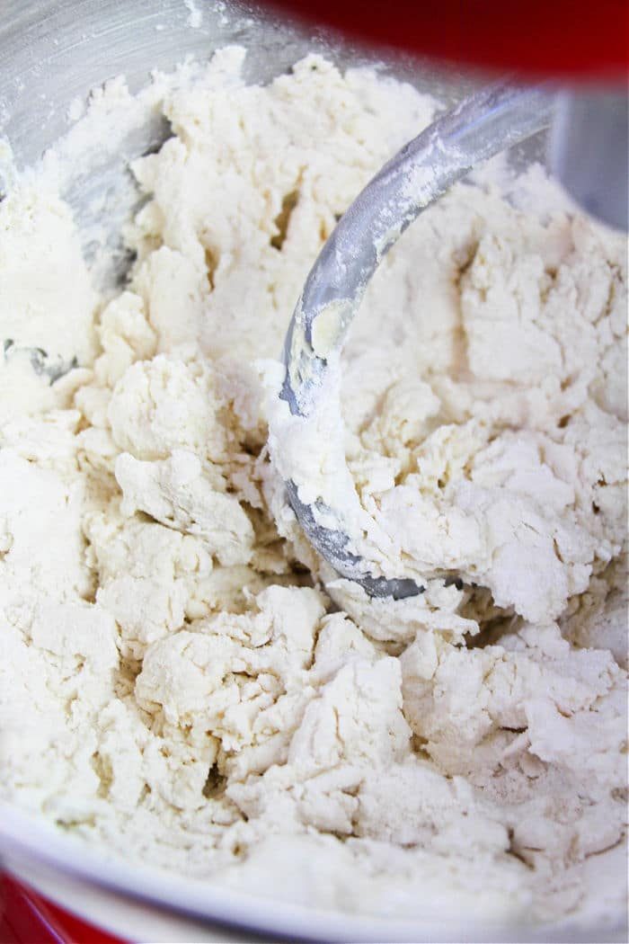 Close-up of biscuit dough being mixed in a metal bowl with a dough hook attachment, similar to the preparation for 2 Ingredient Bagels.