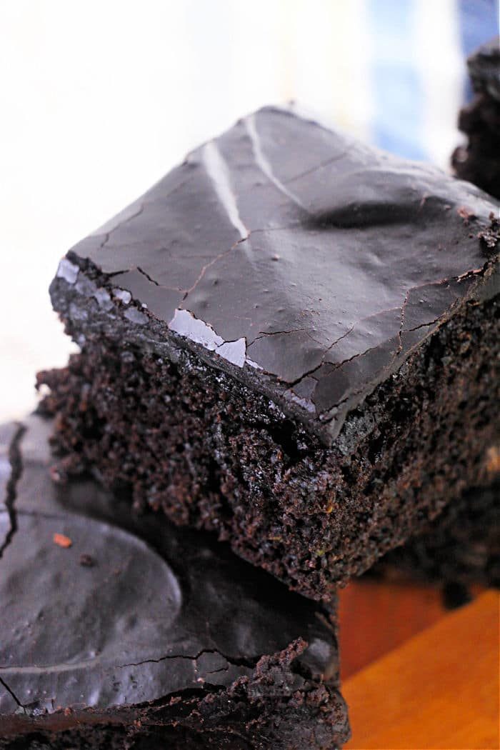 Close-up of a stack of two chocolate brownies on a wooden surface. The brownies, made using a zucchini brownie recipe, have a glossy top with a few cracks, and the texture appears moist and rich.