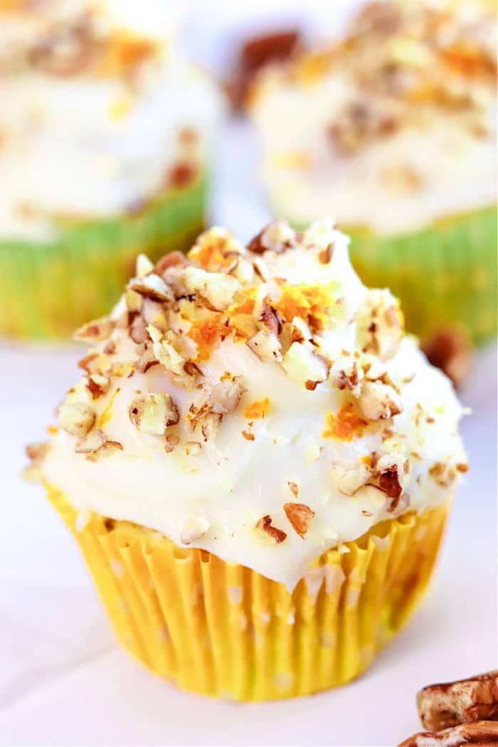 A delightful carrot muffin with cream cheese frosting, sprinkled with chopped nuts, all nestled in a vibrant yellow wrapper. Inspired by the warmth of zucchini carrot muffins, it balances sweetness and texture perfectly.