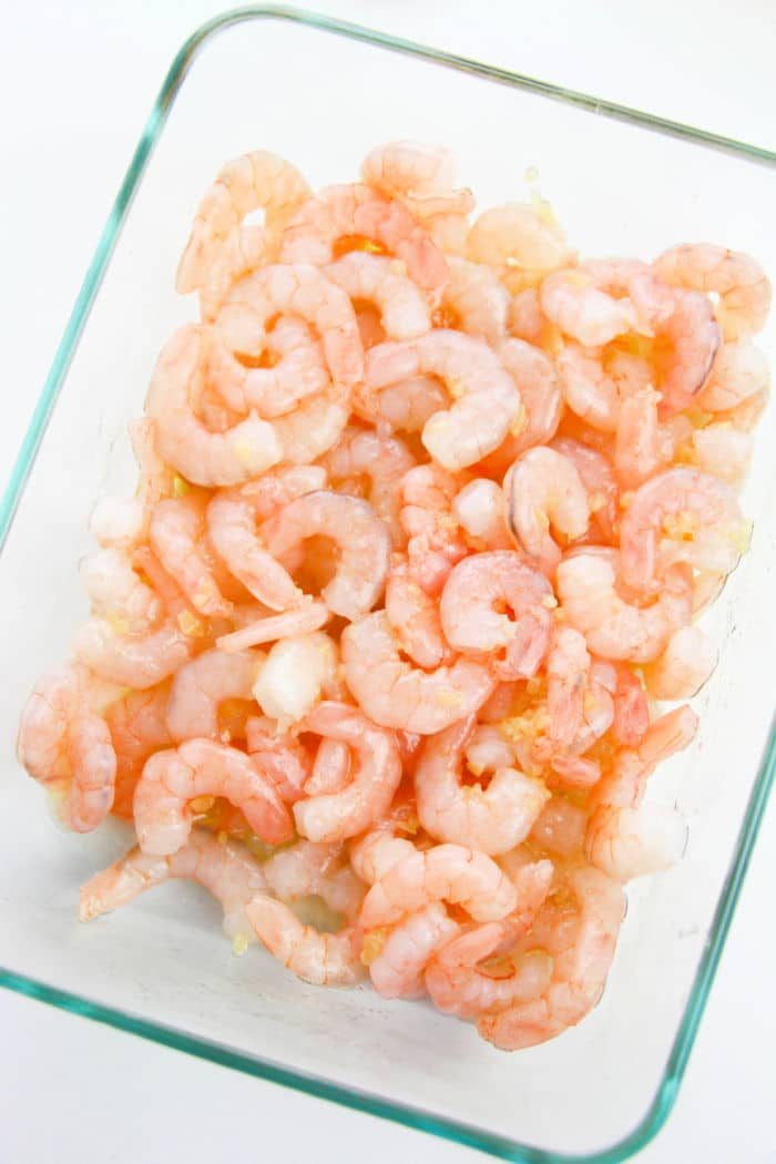 A glass dish filled with raw, peeled shrimp is arranged neatly, ready to transform into a zesty masterpiece.