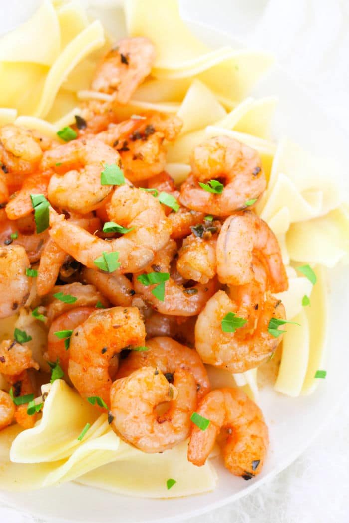 A plate of lemon garlic shrimp pasta garnished with chopped herbs.