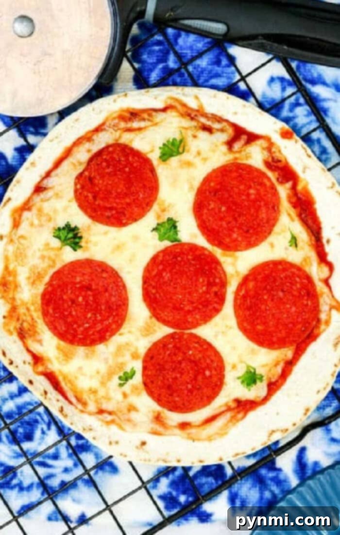 Crispy Air Fryer Tortilla Pizza 2 Two delicious air fryer tortilla pizzas topped with melted cheese and pepperoni, garnished with fresh herbs, resting on a wire rack, ready to be served as a quick and easy meal.