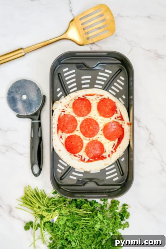 Crispy Air Fryer Tortilla Pizza 5 A hand carefully placing a fully topped tortilla pizza into an air fryer basket, demonstrating the easy cooking process for homemade air fryer tortilla pizzas.