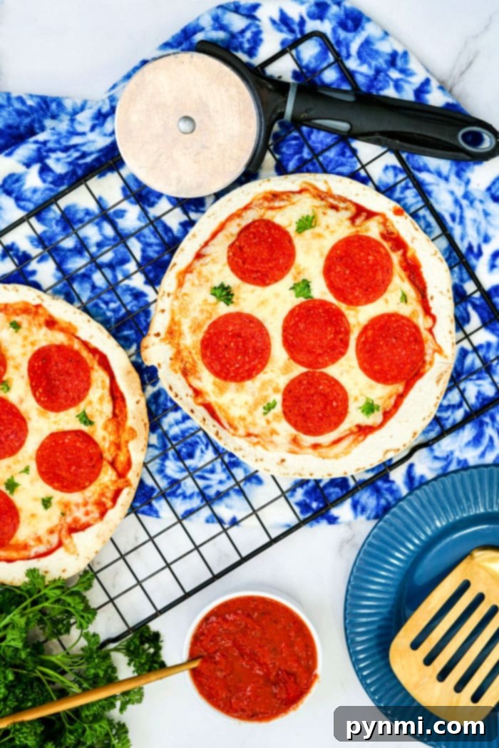 Crispy Air Fryer Tortilla Pizza 6 Two perfectly cooked Air Fryer Tortilla Pizzas resting on a cooling rack, accompanied by a pizza cutter, a bowl of sauce, and serving utensils, highlighting they are ready to be served and enjoyed by the family.