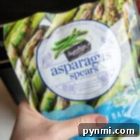 A hand holds a package of Signature Select frozen asparagus spears, perfect for the air fryer.