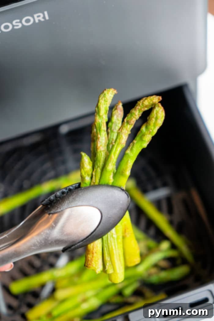 Crispy Air Fryer Frozen Asparagus 2 Air Fryer Frozen Asparagus spears cooking to perfection in an air fryer basket, with steam rising.