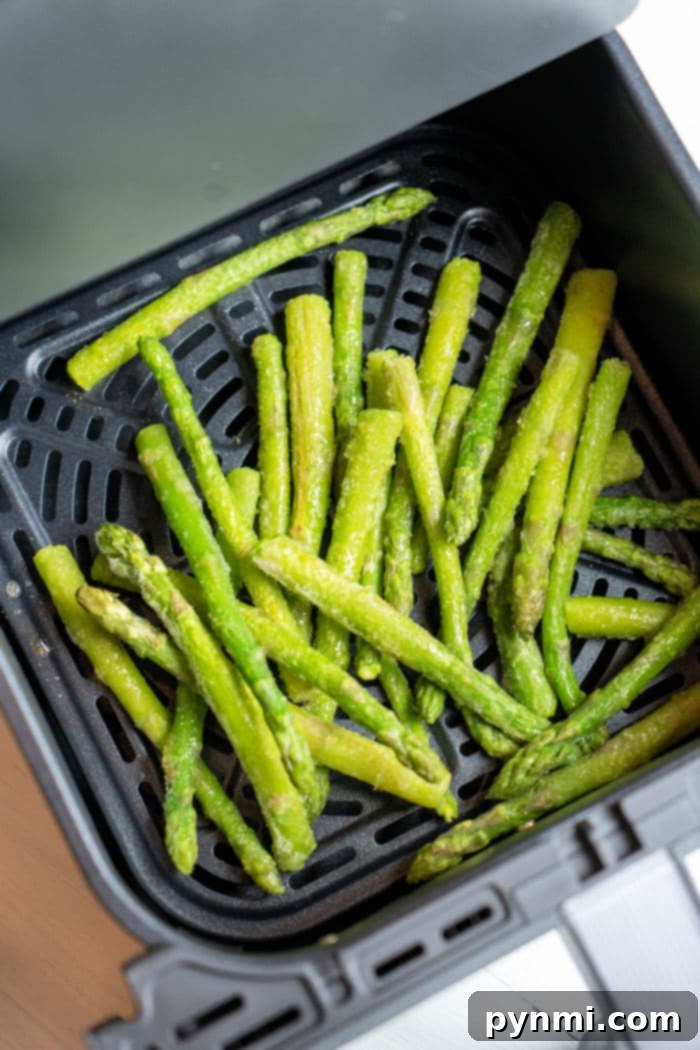 Crispy Air Fryer Frozen Asparagus 4 Frozen asparagus being poured into an air fryer basket, ready for cooking.
