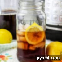 Golden Sweetness: Lipton Tea Brew 6 A mason jar filled with iced tea and a lemon slice sits amidst fresh lemons, hinting at the secret of how to make sweet tea with Lipton tea bags. An appliance hums softly in the background, promising more refreshing sips to come.