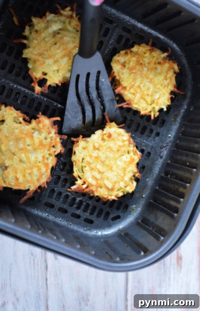 Close-up of golden brown latkes cooking in an air fryer basket, showing their crispy texture.