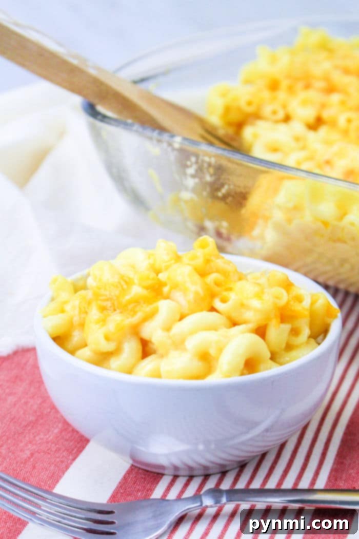 A golden brown, baked mac and cheese, reminiscent of Chick-fil-A's classic side, served in a clear glass dish, with a wooden spatula ready for serving. A festive red and white striped cloth sits underneath the dish.