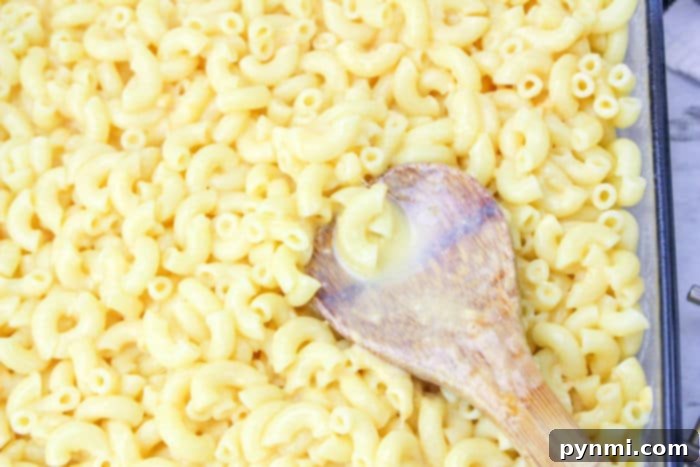 Hands stirring the creamy, golden cheese sauce with cooked elbow macaroni in a large pot, illustrating how to make Chick Fil A Mac and Cheese.