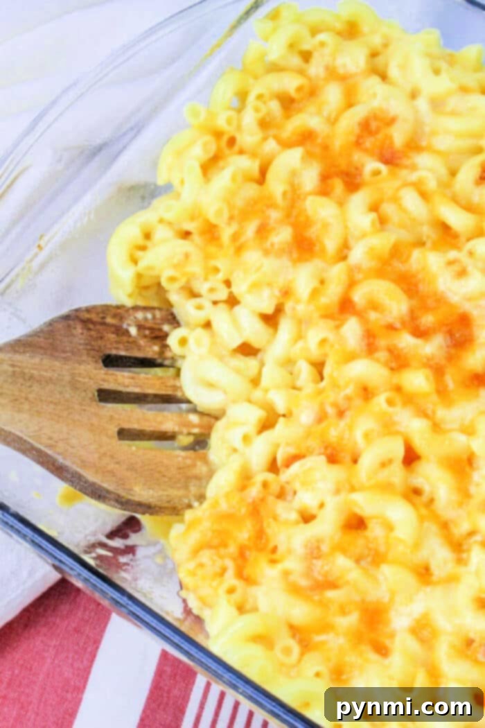 Baked mac and cheese, reminiscent of a Copycat Chick Fil A Mac and Cheese, sits invitingly in a glass dish with a wooden spatula on a red and white cloth.