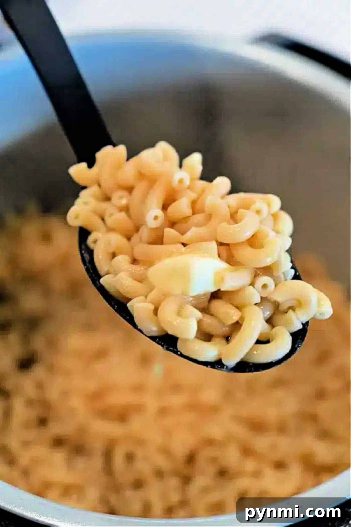 A spoonful of cooked elbow macaroni with a piece of butter, held over a pot of more macaroni—perfect for making creamy Ninja Foodi Butter Noodles.