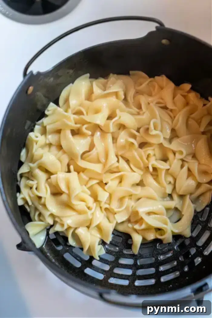 Cooked pasta noodles glisten in a black colander, showcasing their glossy texture from above. Their silky appearance suggests they've been transformed into delicious Ninja Foodi butter noodles, capturing the essence of creamy perfection as they rest in the strainer.
