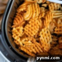 Frozen waffle fries sizzle to perfection in an open air fryer basket, with a floral-patterned cloth elegantly poised beside it.