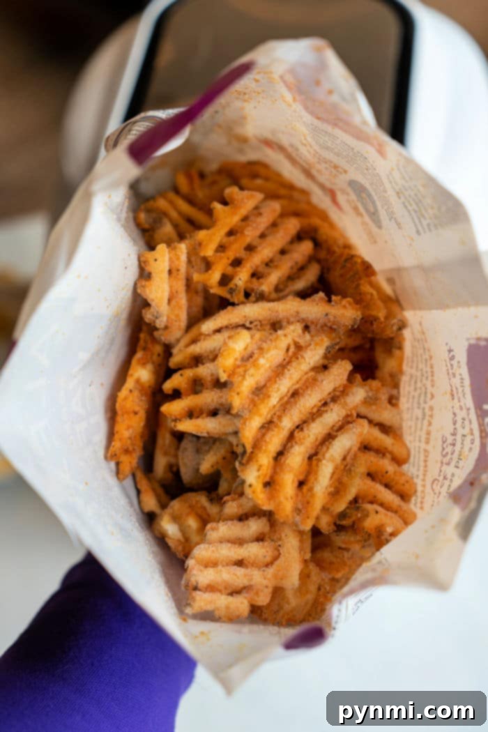 A person proudly holds a bag of frozen seasoned waffle fries, perfectly crispy from the air fryer.