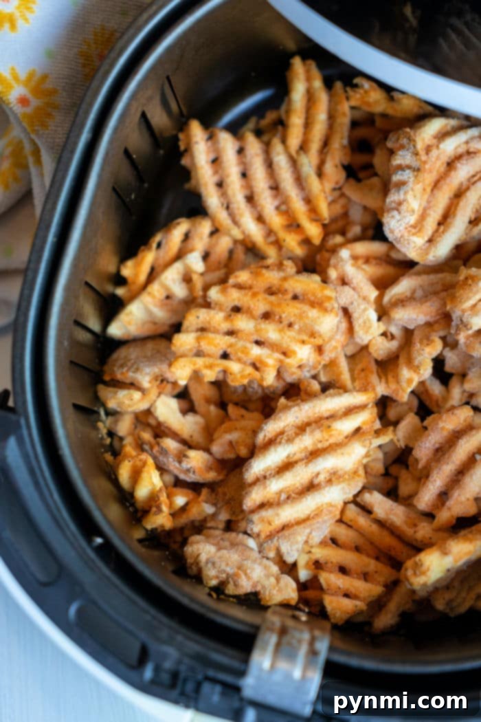 Close-up of golden, crispy frozen waffle fries in an air fryer basket.