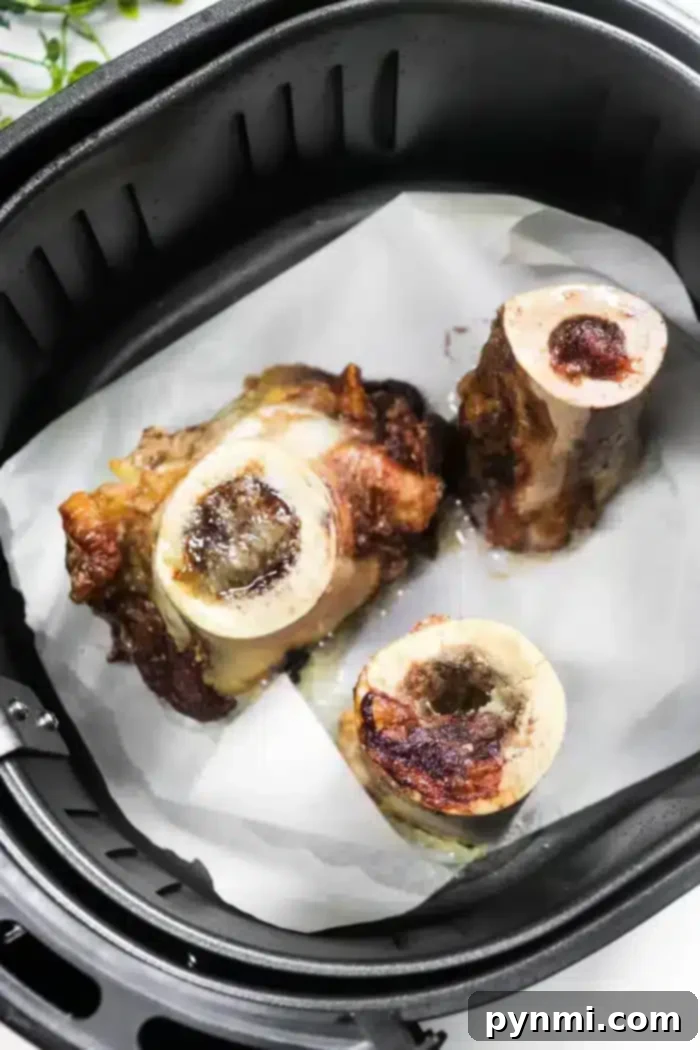 Golden Air-Fried Bone Marrow 2 Three pieces of roasted air fryer bone marrow sit perfectly on a sheet of parchment paper inside the basket, their surfaces golden and slightly charred.
